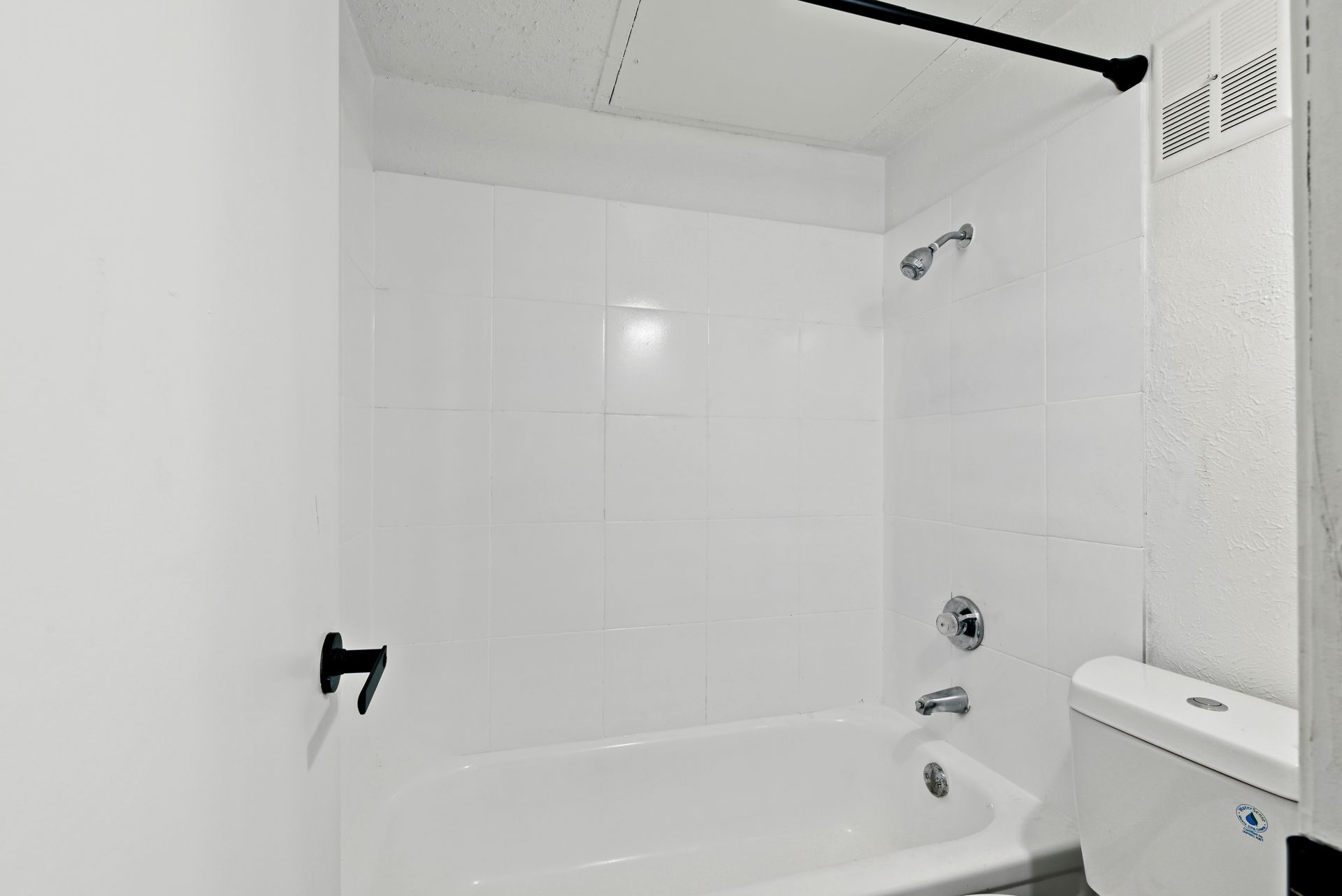 White-tiled bathroom with tub, toilet, and showerhead. Black accents on fixtures.