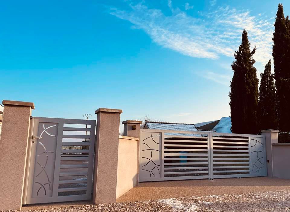 Un ensemble portail grande largeur motorisé et son portillon dans une teinte gris claire ( Gris 2400 sablé)