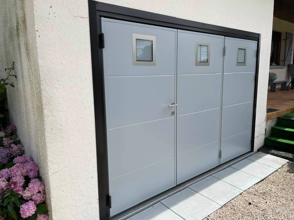 Porte de garage lumineuse grâce aux trois hublots installée par TRIHOME Menuiseries à Saint-Germain-du-Bois.