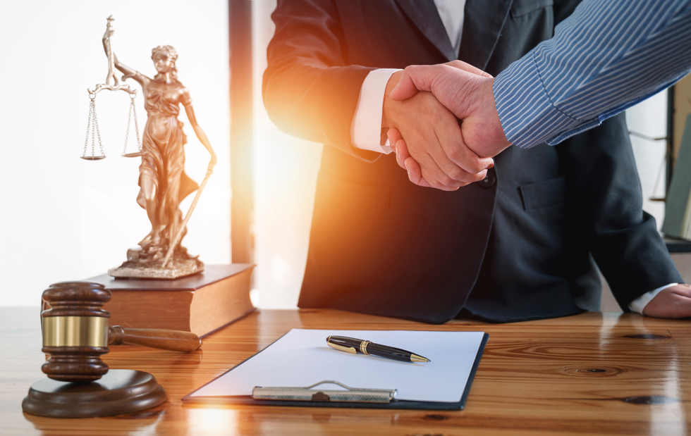 Two men are shaking hands in front of a statue of justice.