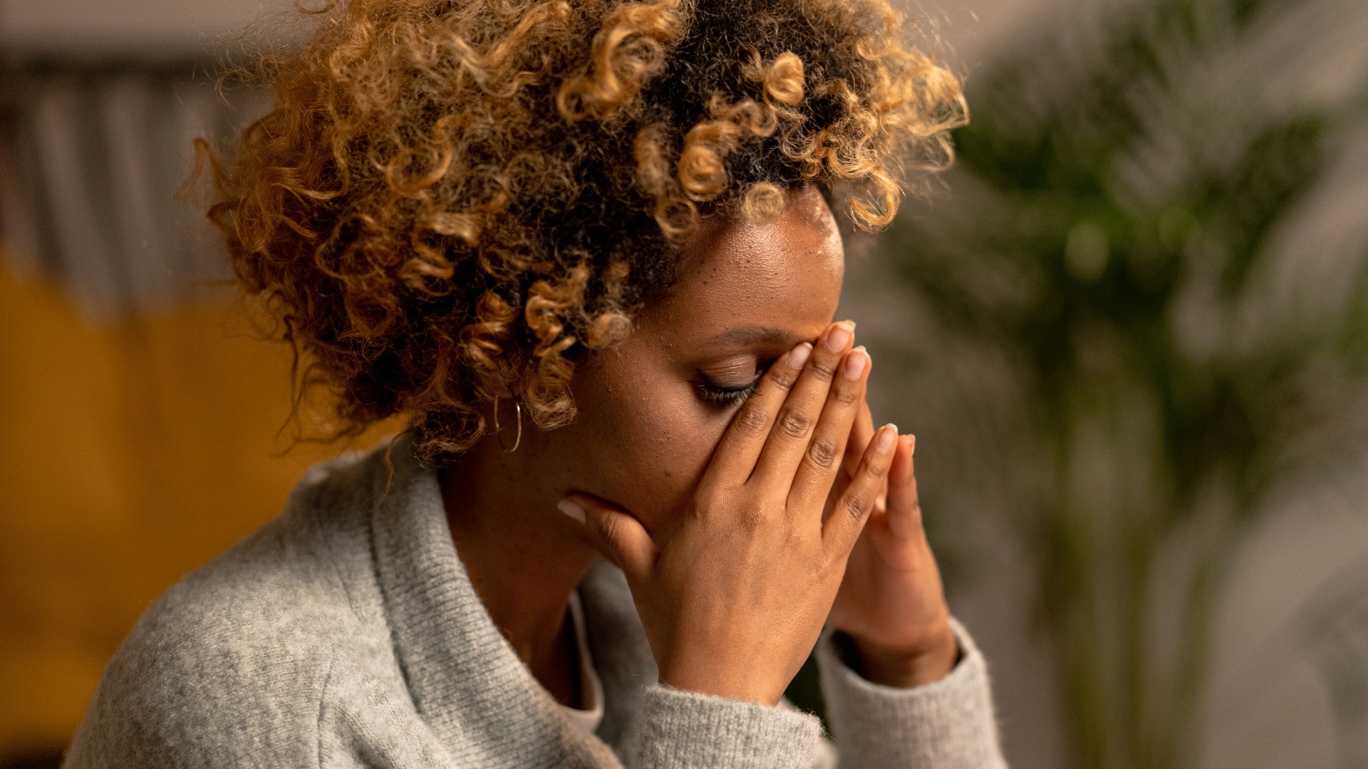 A woman with curly hair is covering her face with her hands.