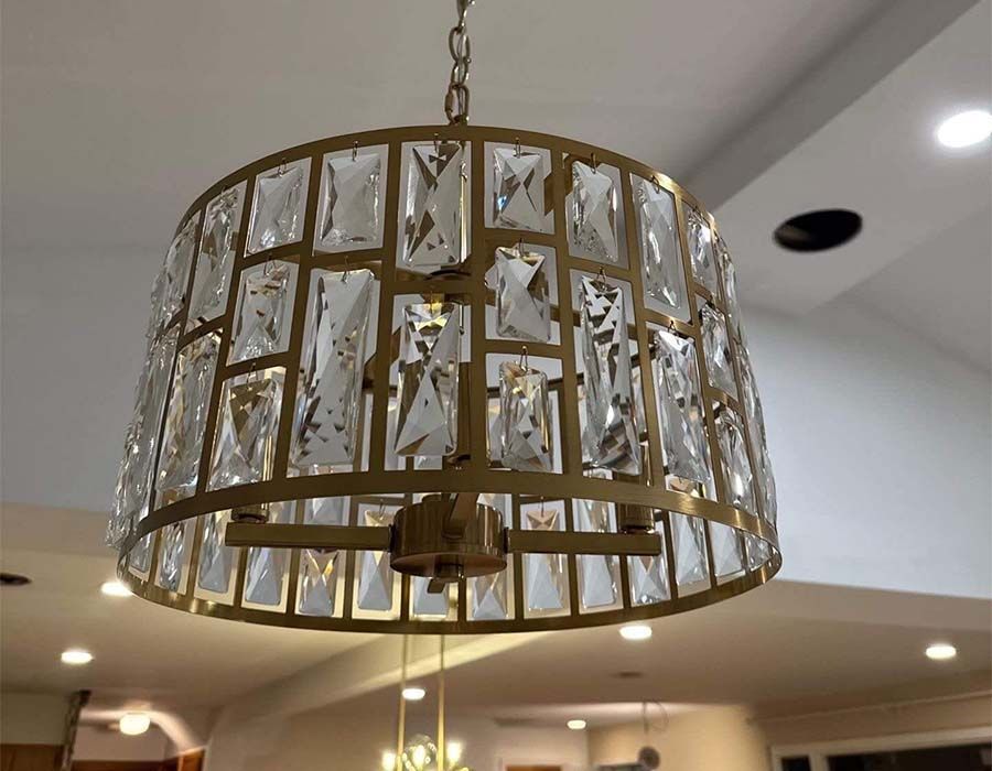 A gold-toned drum chandelier featuring rectangular crystal accents, suspended from a ceiling in an indoor room.