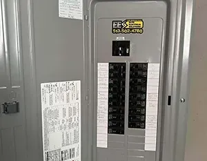A grey electrical circuit breaker panel with a sticker for EES Electrical Solutions featuring a contact phone number.