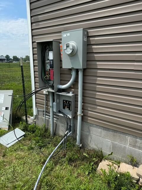 An outdoor electrical meter assembly mounted on a building's vinyl siding above a concrete block foundation.