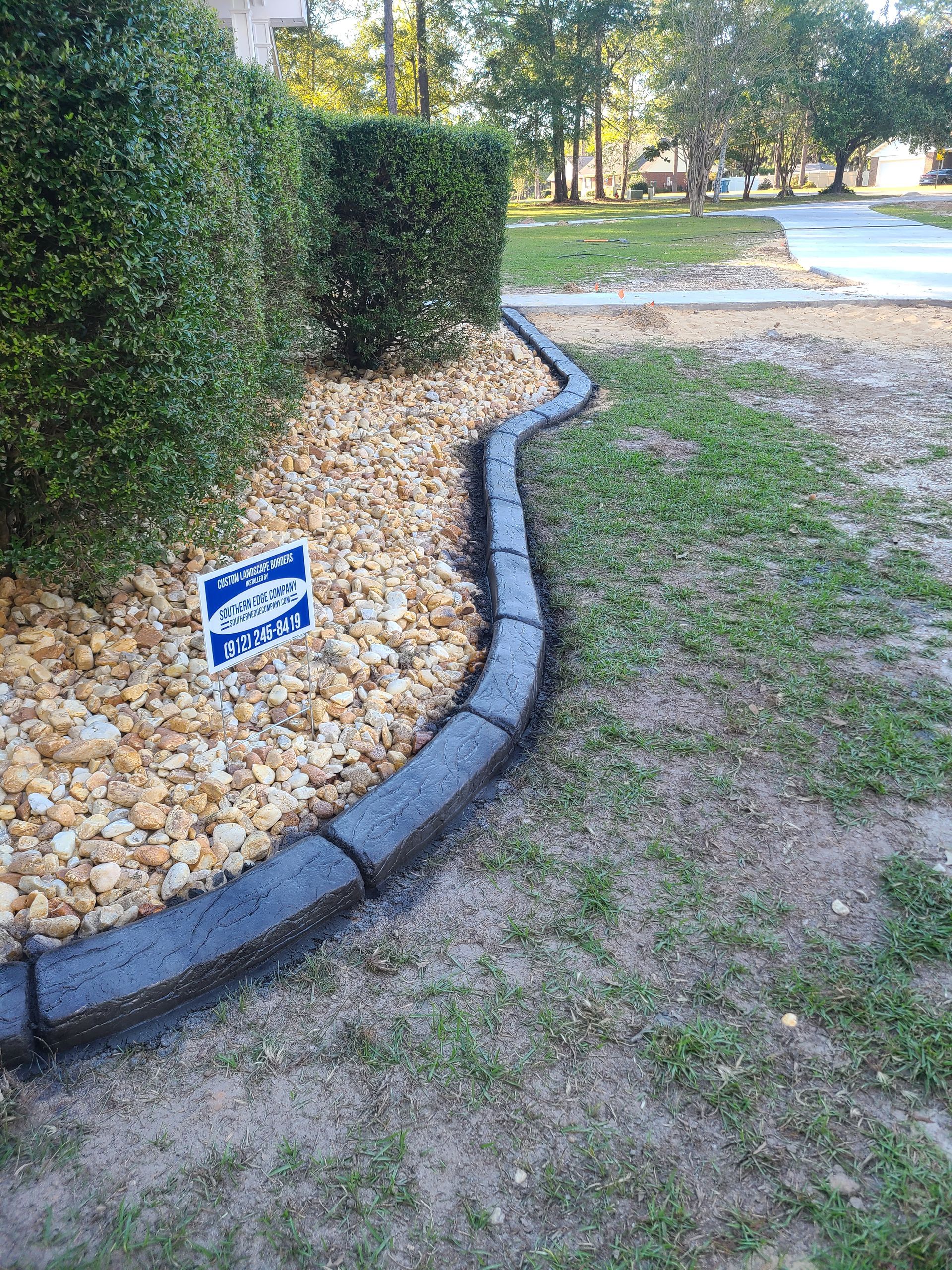 A concrete curb is surrounded by rocks and a sign.