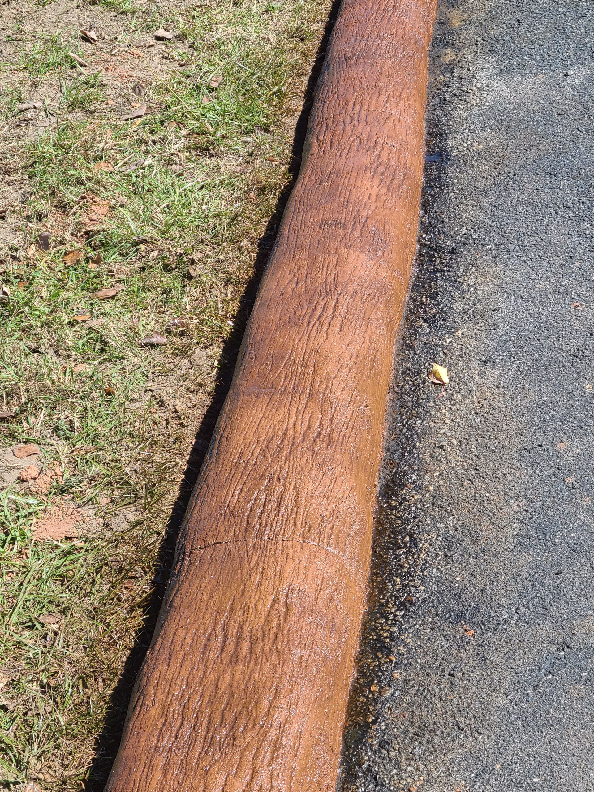 A rusty pipe is sitting on the side of a road next to a grassy area.