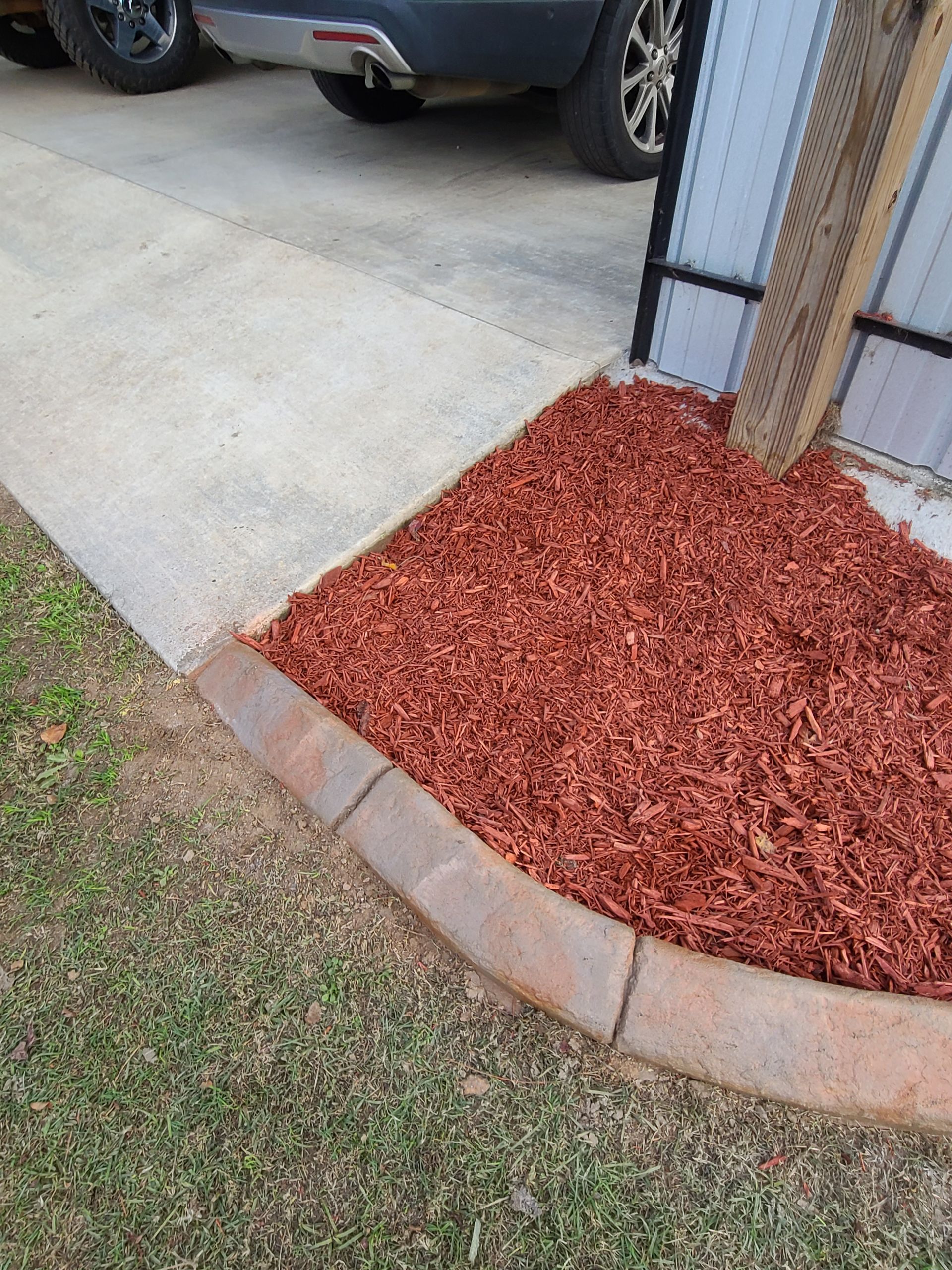A sidewalk with red mulch and a car parked in the background.