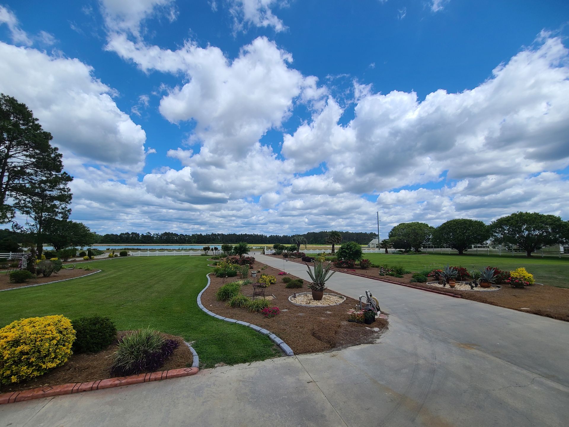 A driveway leading to a large grassy field with a lake in the background