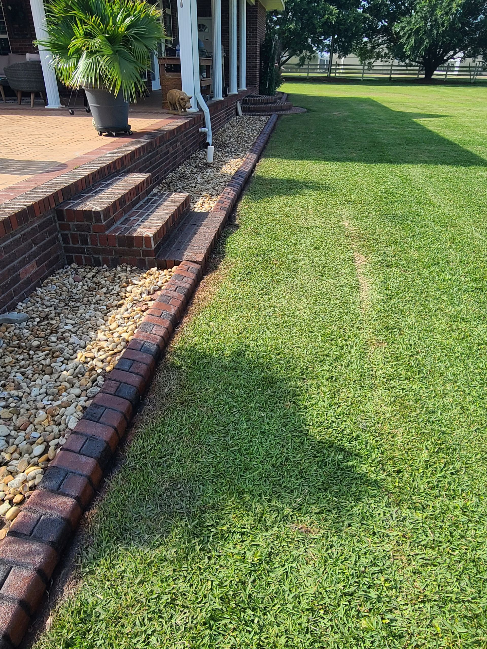 A lush green lawn with a brick walkway leading to a house.