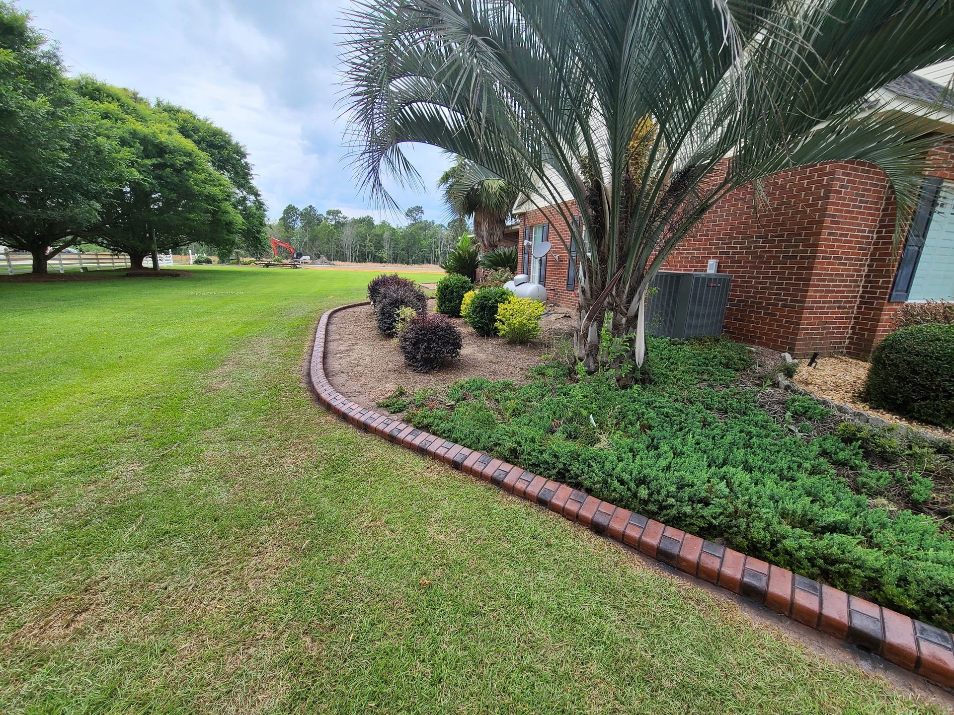 A lush green lawn with a brick curb in front of a brick house.