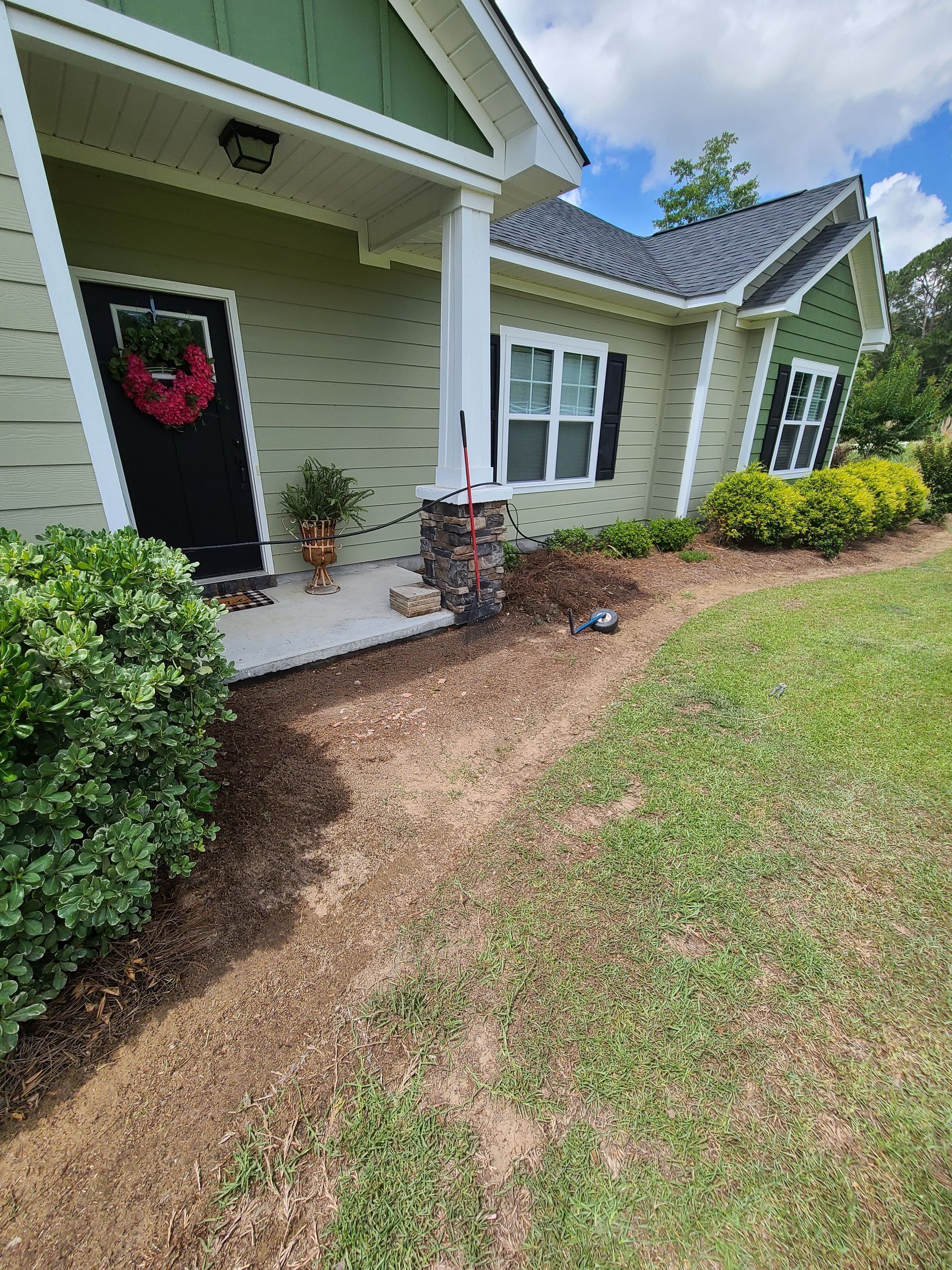 A green house with a black door and white trim is sitting on top of a lush green lawn.