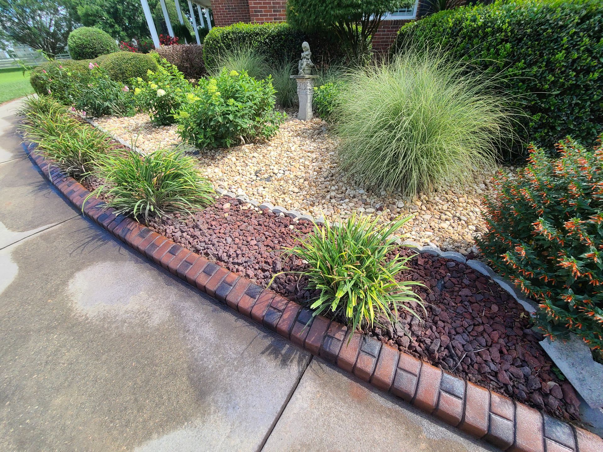 A brick walkway leading to a garden with lots of plants and rocks.