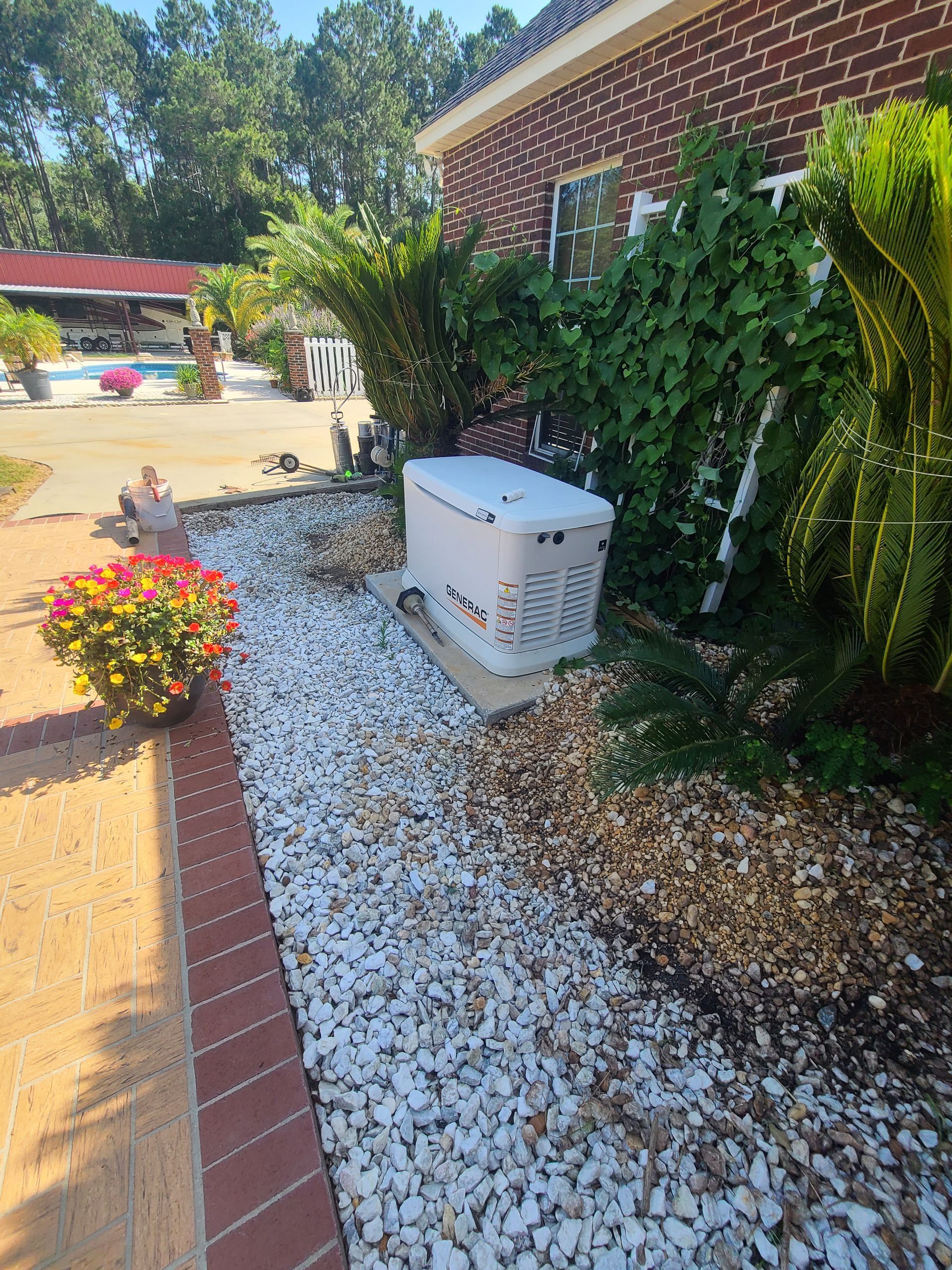 A generator is sitting in the gravel in front of a brick house.