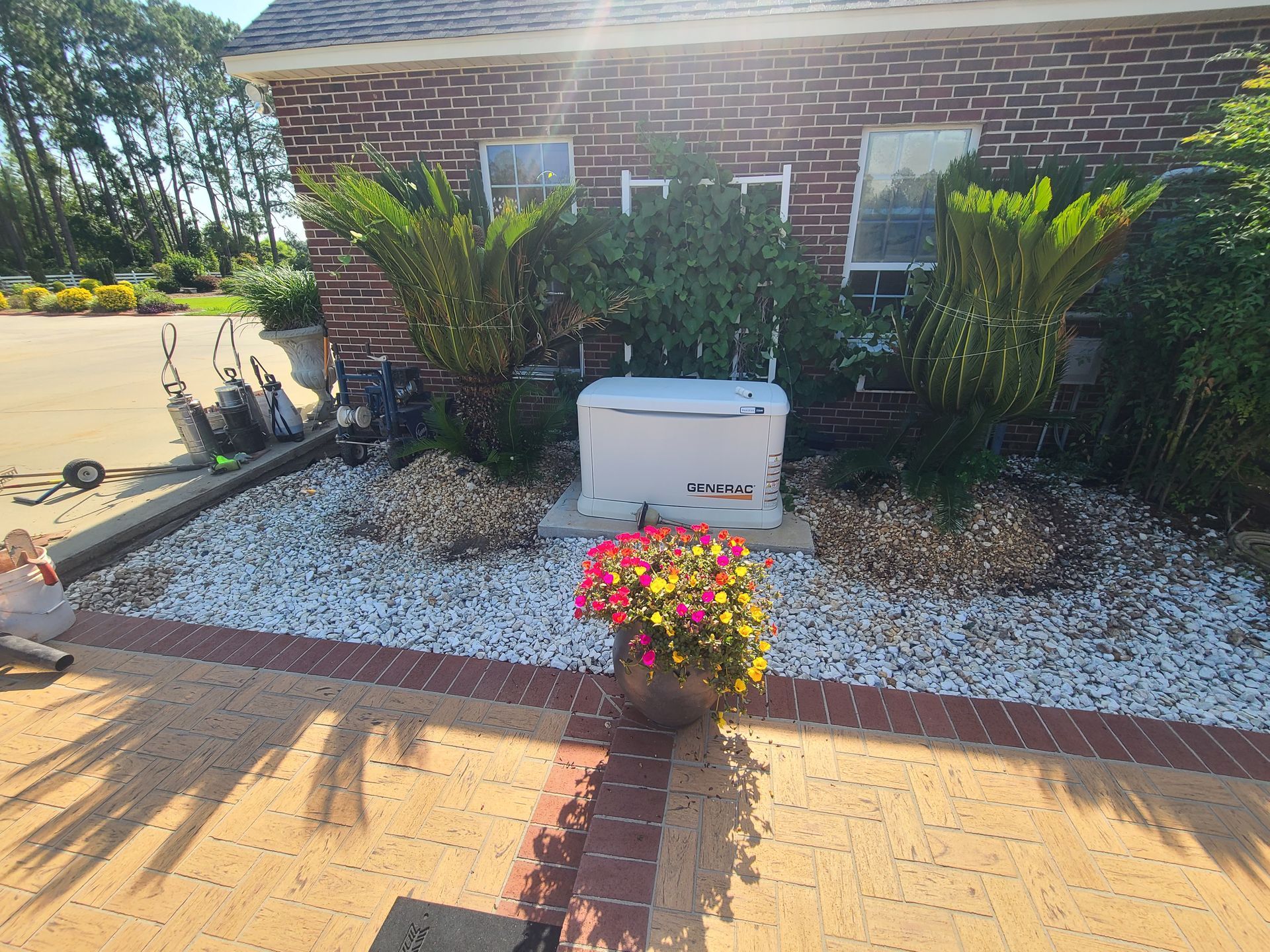 A white box is sitting in front of a brick house surrounded by flowers.