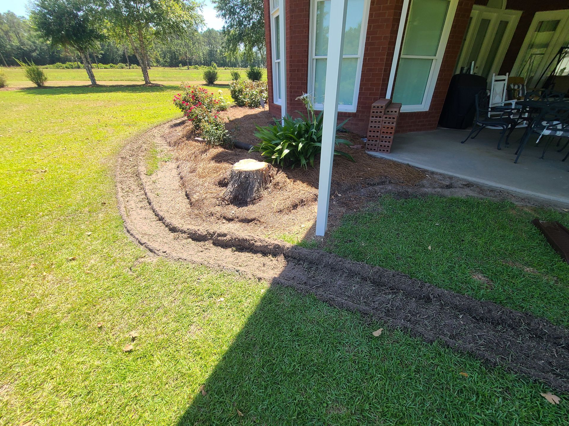 A stump in the middle of a lush green lawn in front of a house.