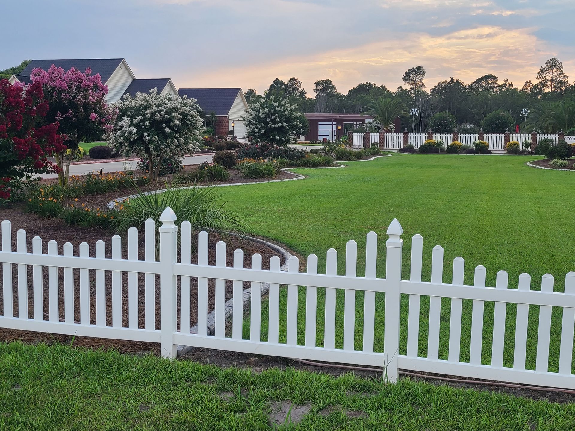 A white picket fence surrounds a lush green field