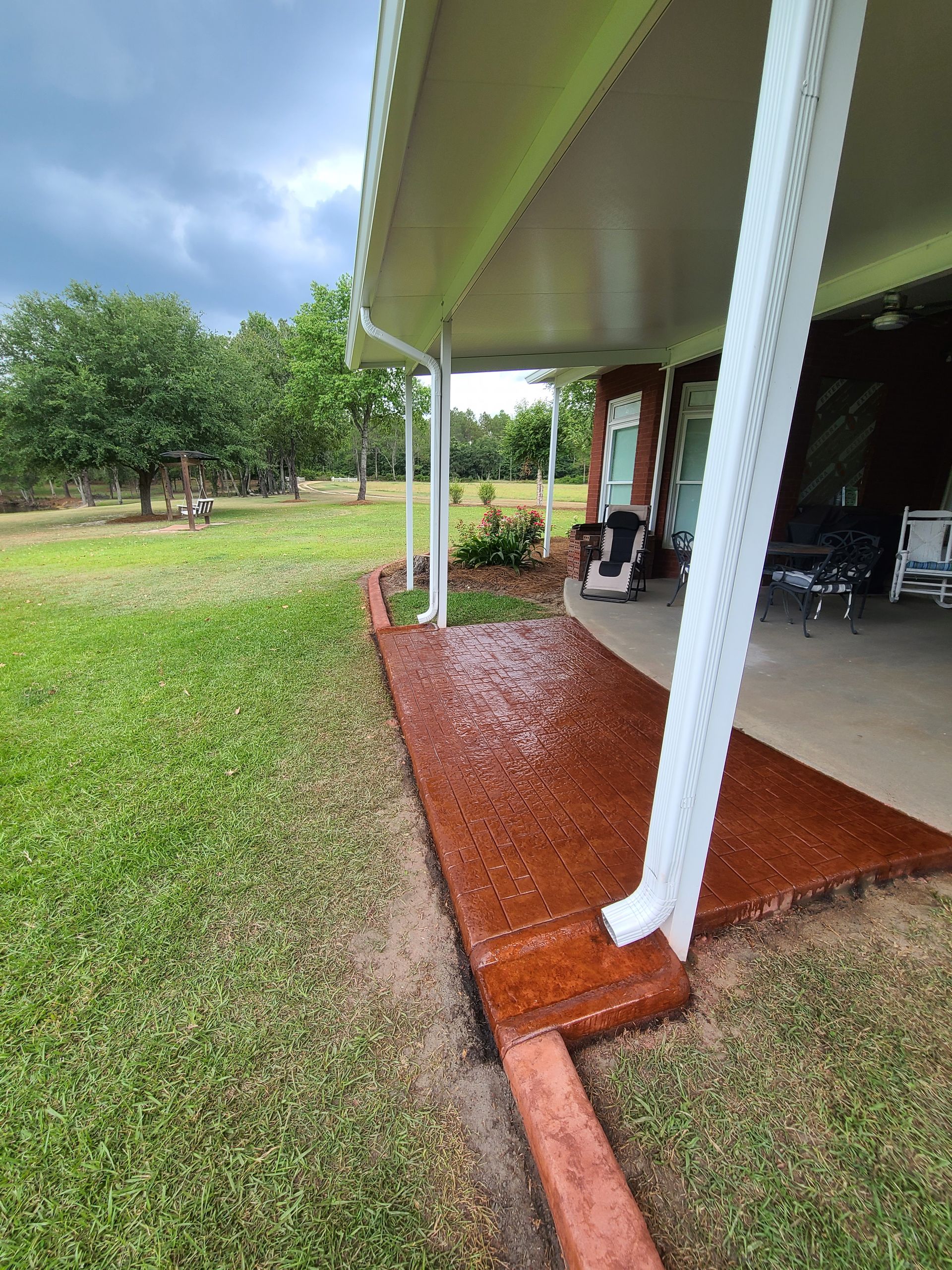 A covered porch with a concrete walkway leading to it.