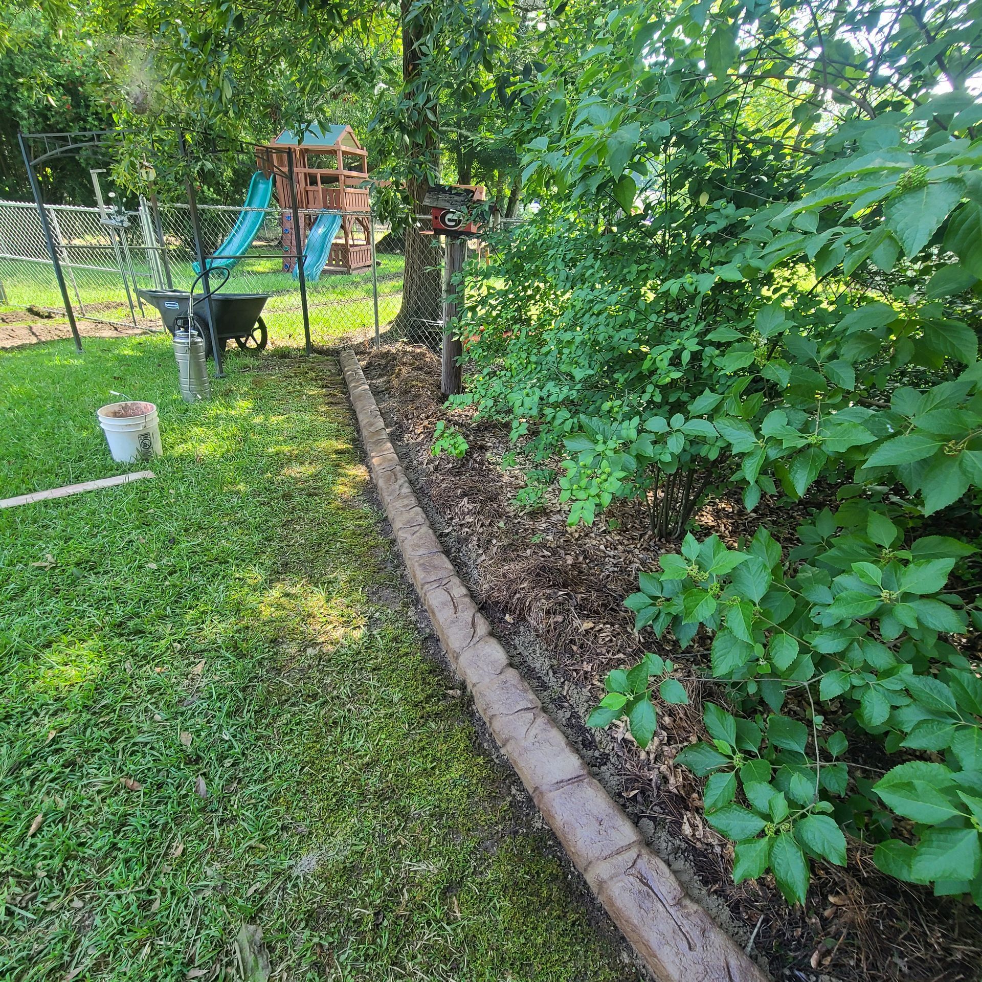 A backyard with a concrete curb and a playground in the background.