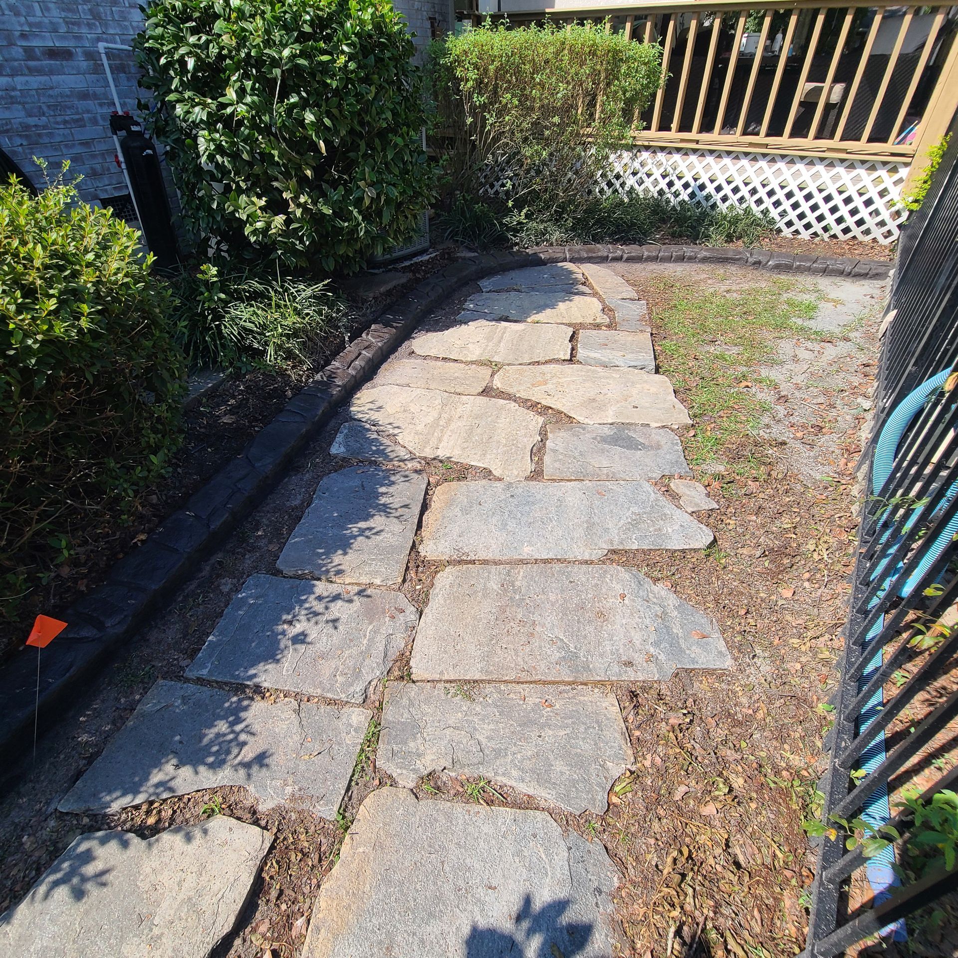 A stone walkway in a backyard next to a fence and a hose.