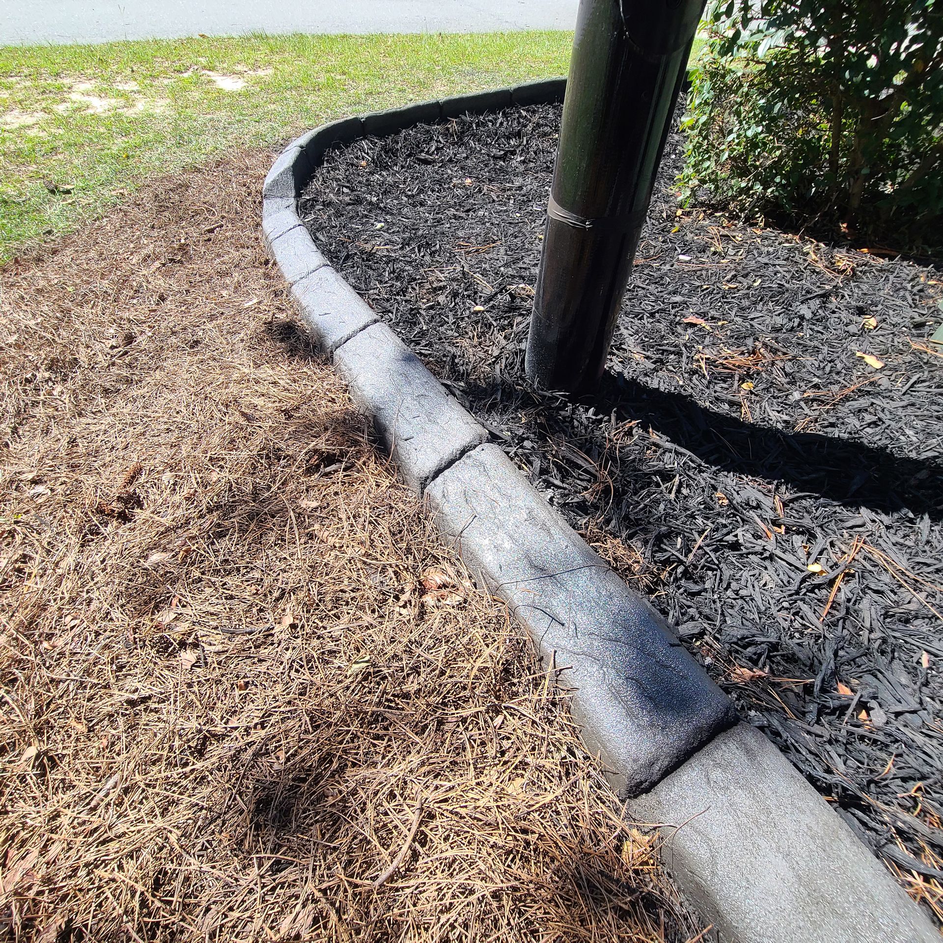 A concrete curb is sitting on top of a pile of mulch next to a tree.