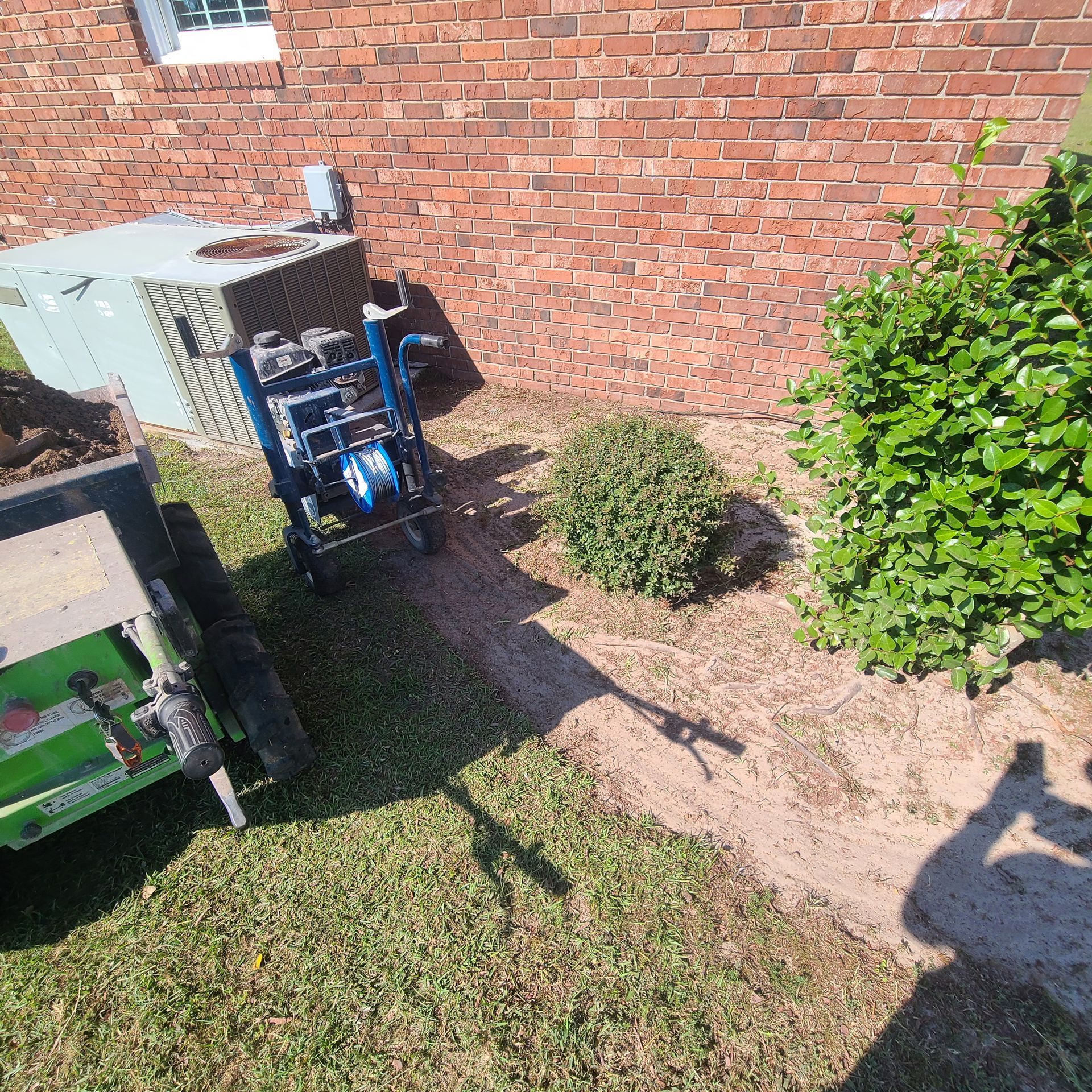 A lawn mower is sitting in the grass next to a brick wall.