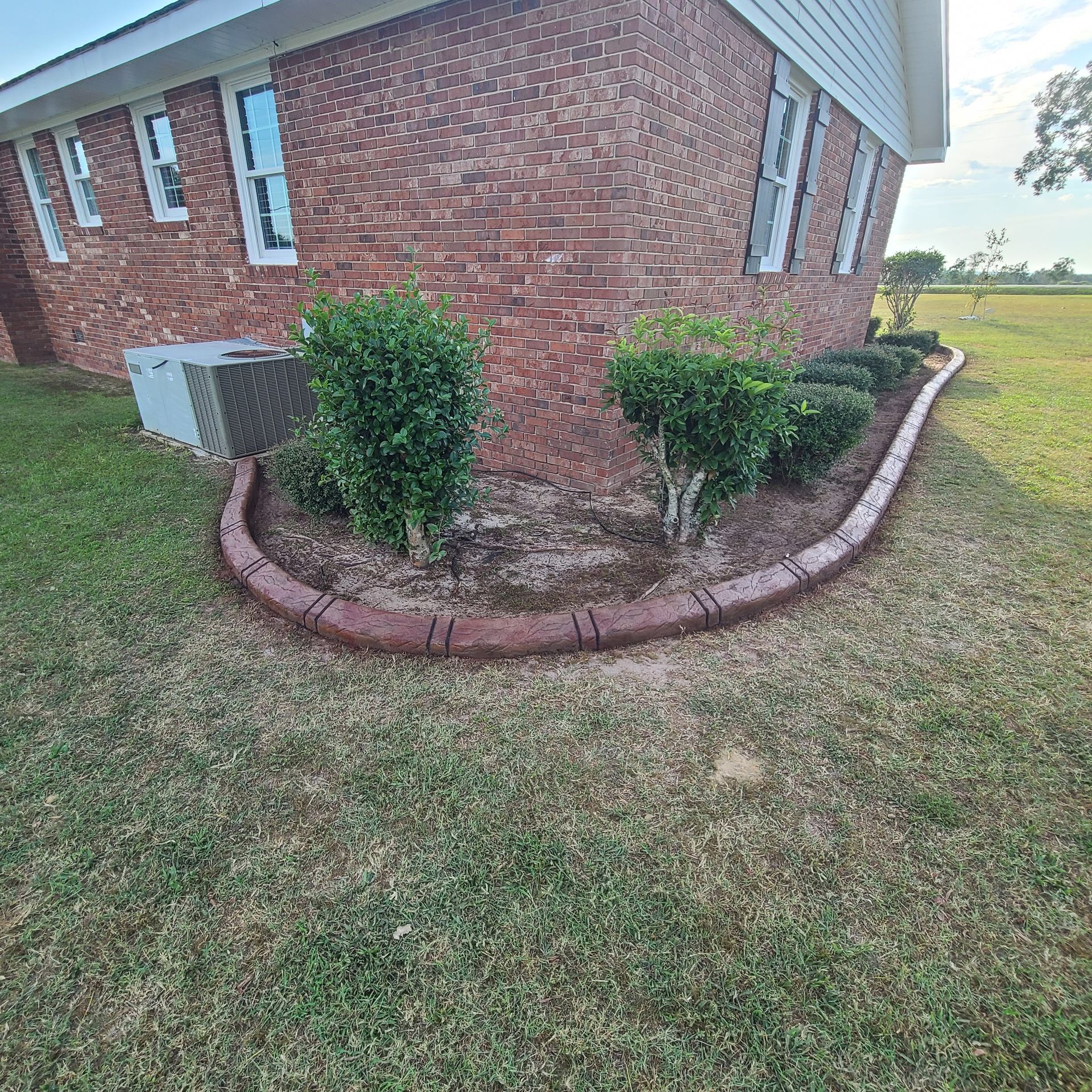 A brick house with a concrete curb and bushes in front of it.