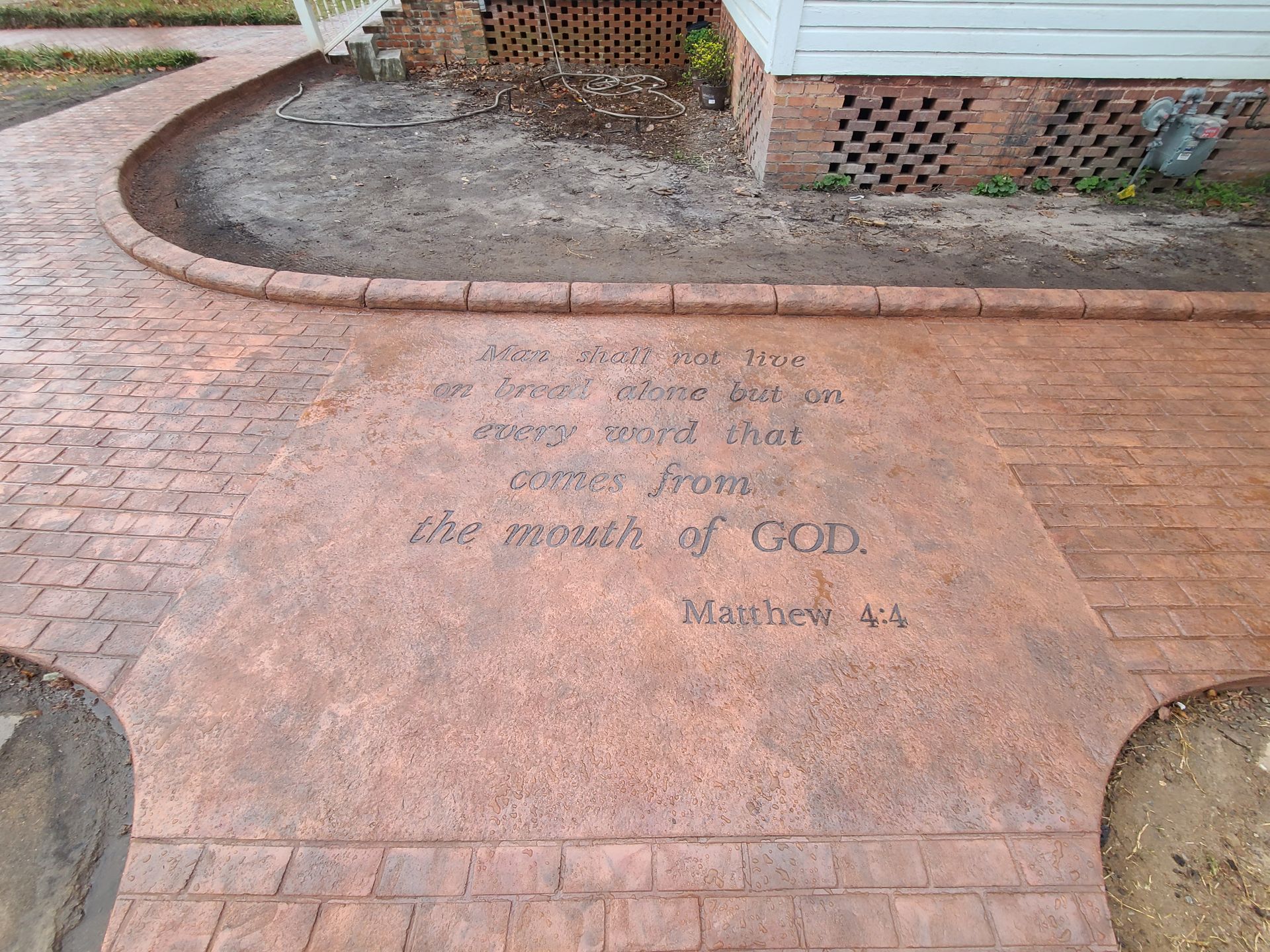 A brick walkway with a bible verse on it in front of a house.