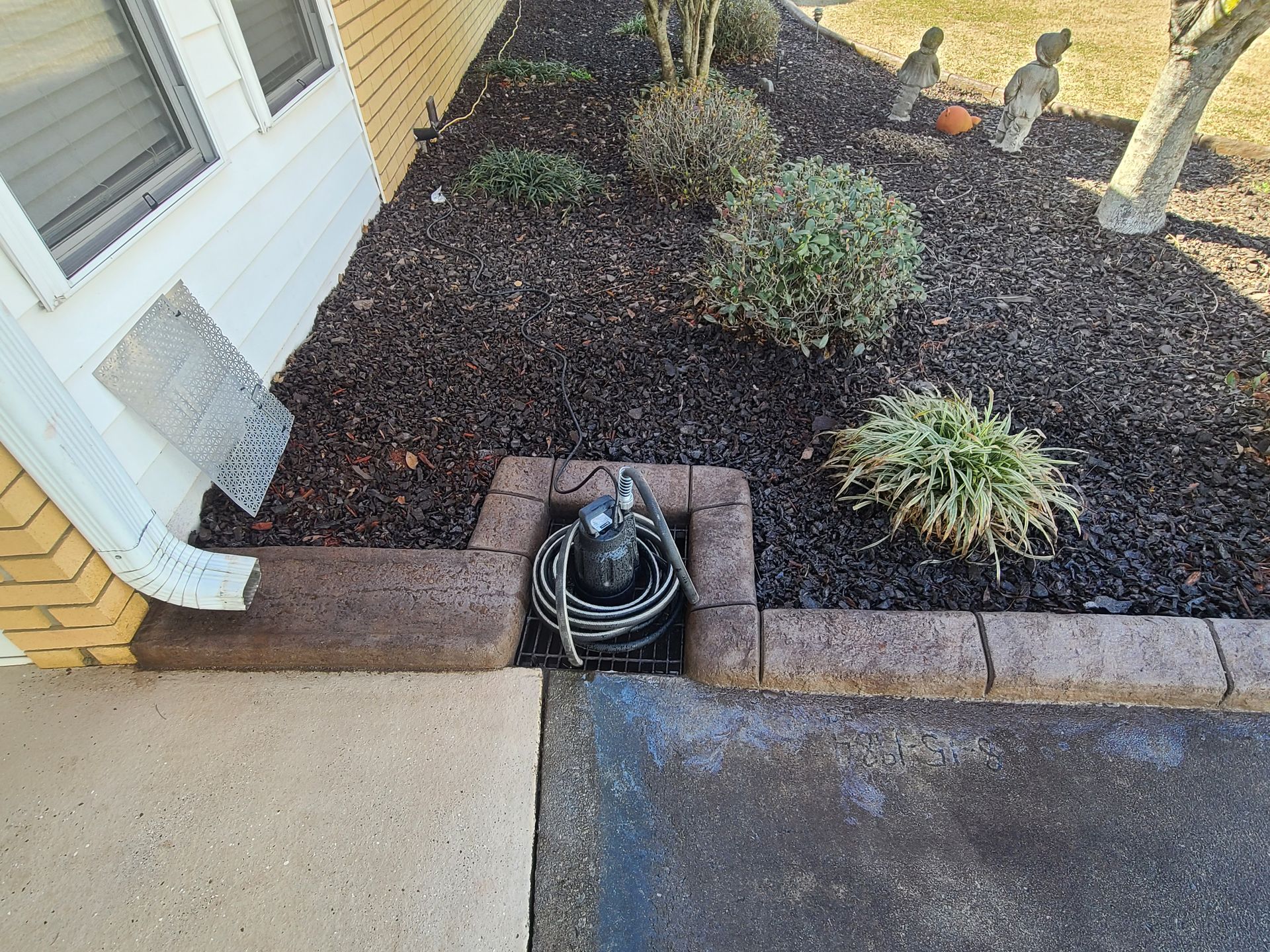 A hose is sitting in a hole in the ground next to a house.
