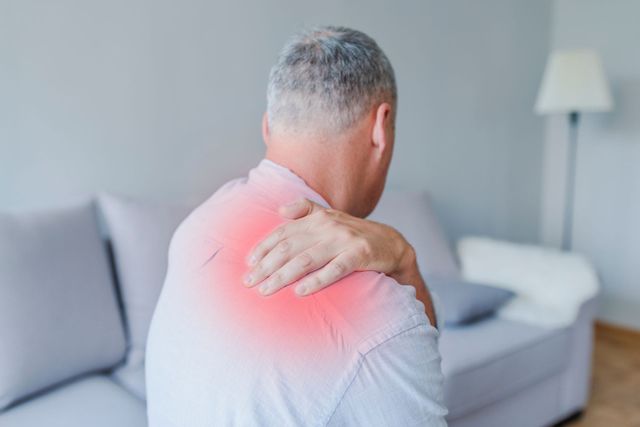 A man is sitting on a couch holding his shoulder in pain.