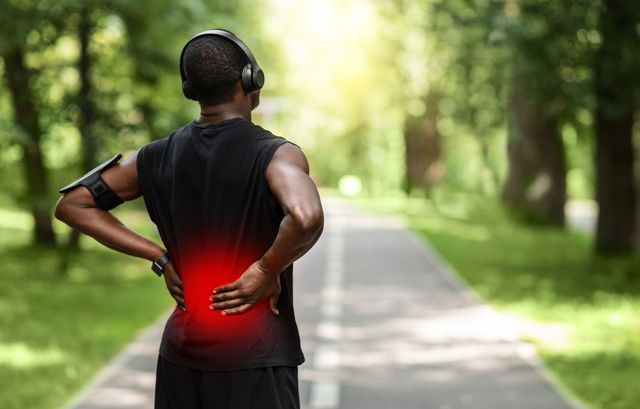 A man wearing headphones is holding his back in pain.