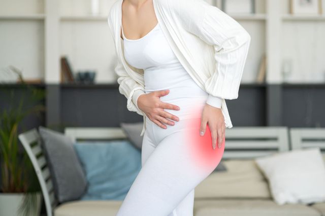 A woman is holding her hip in pain in a living room.