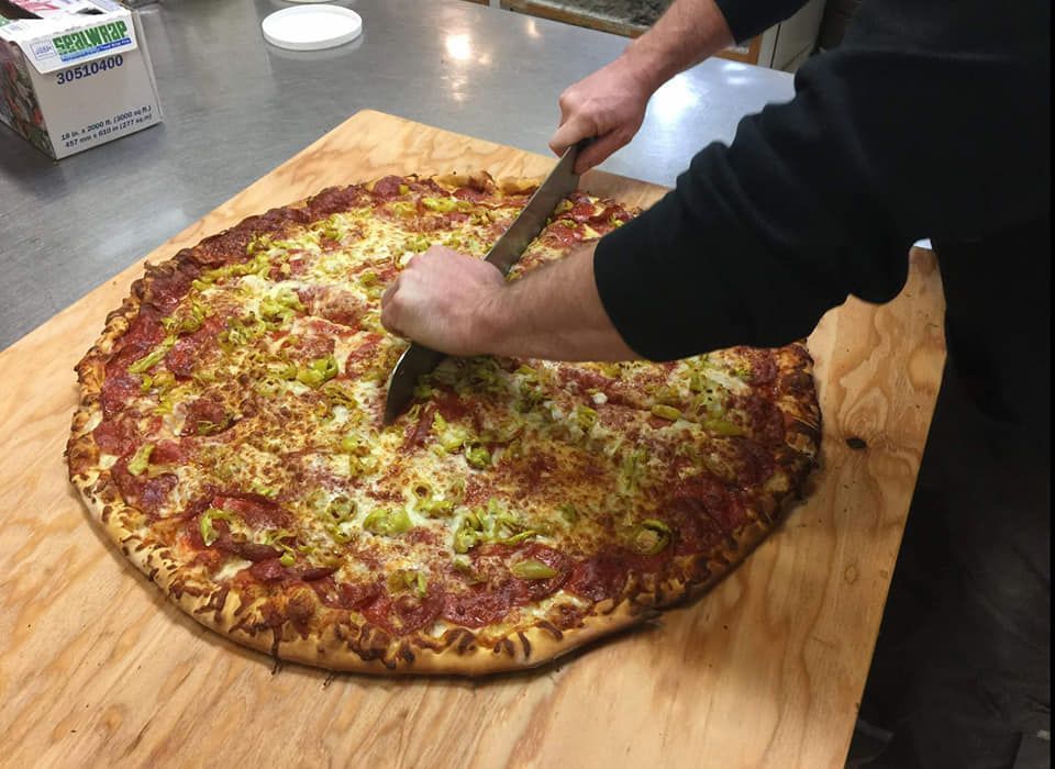 Person Cutting a Large Pizza on A Wooden Cutting Board