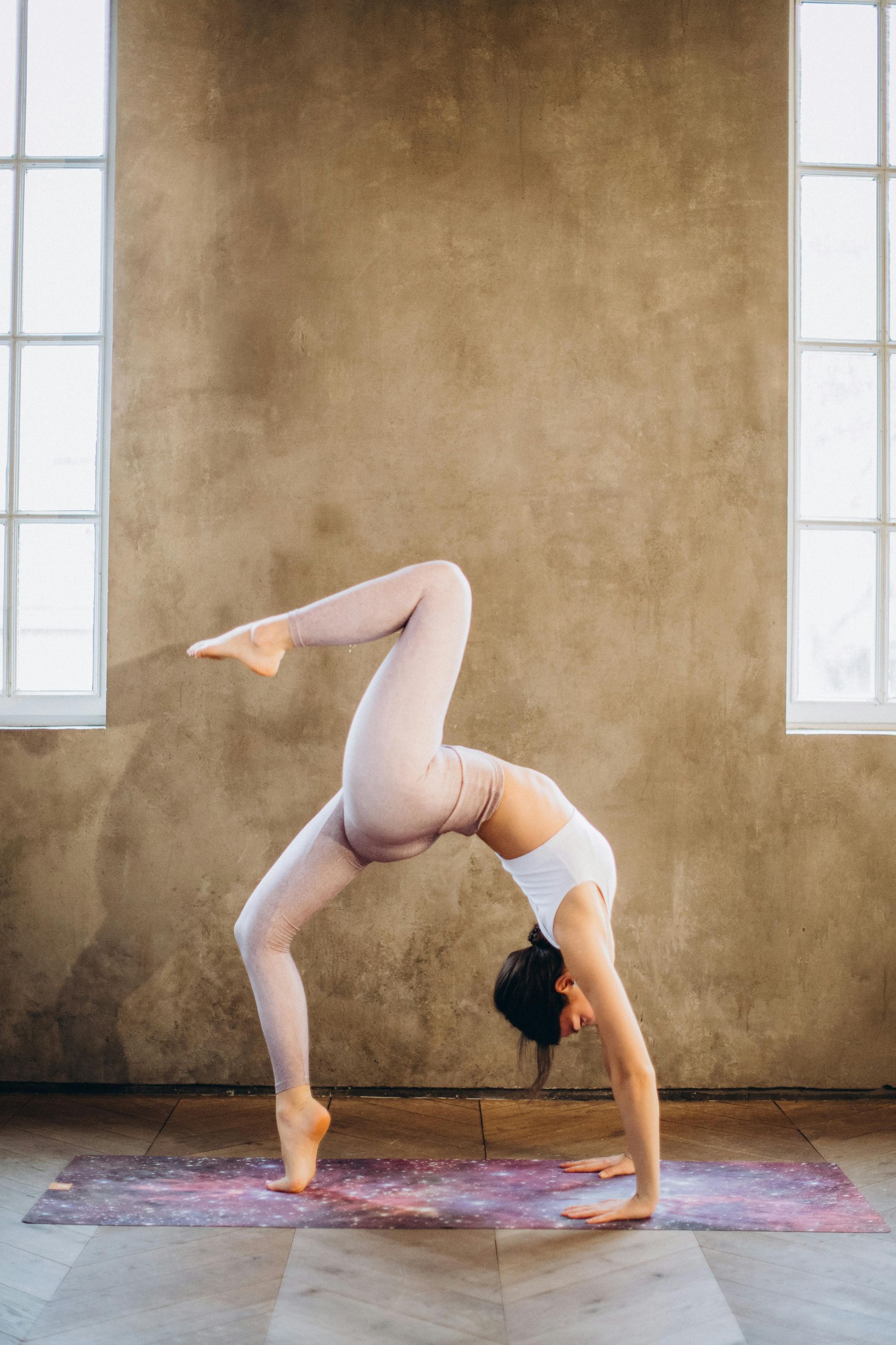 Woman in a bridge pose, leg lifted, on a yoga mat. Indoors, neutral tones.