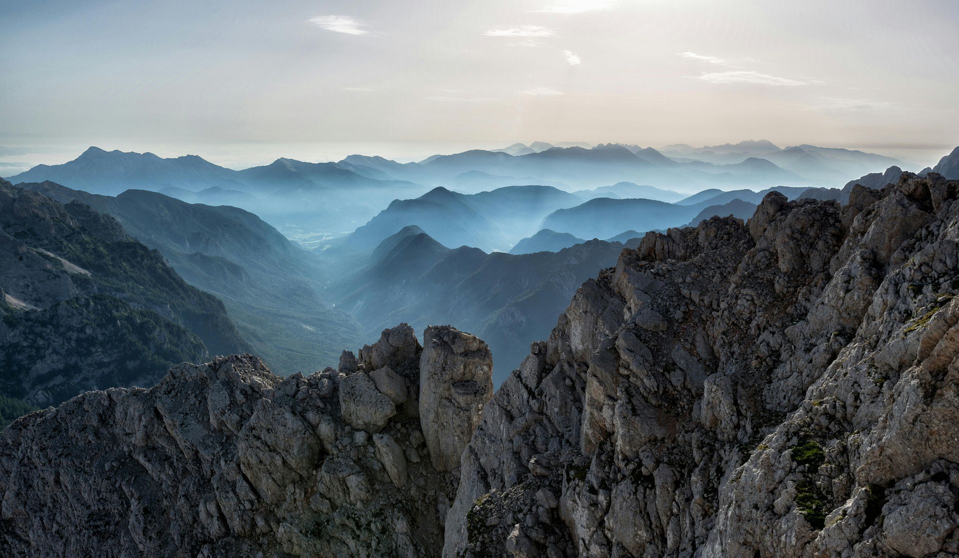 Jagged mountain ridges in layers, fading into a hazy blue distance under a pale sky.
