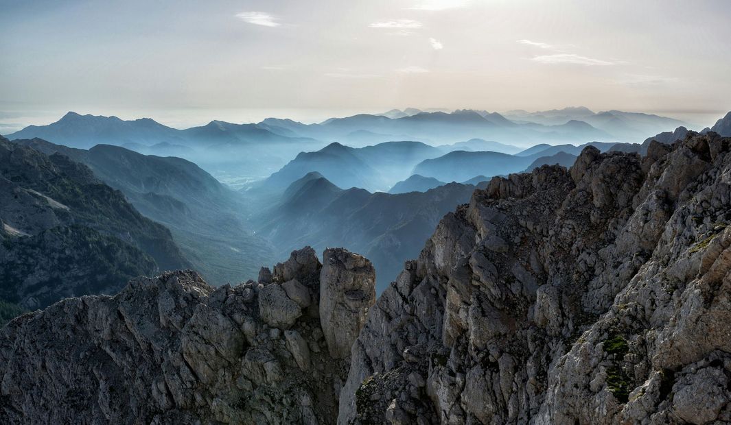 Jagged mountain ridges in layers, fading into a hazy blue distance under a pale sky.