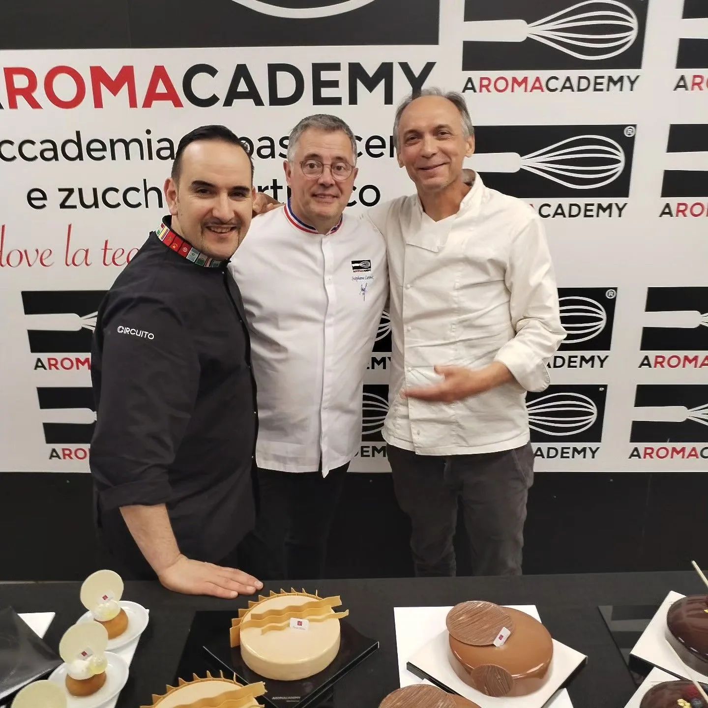 Tre chef sorridenti posano davanti a una parete con il marchio 