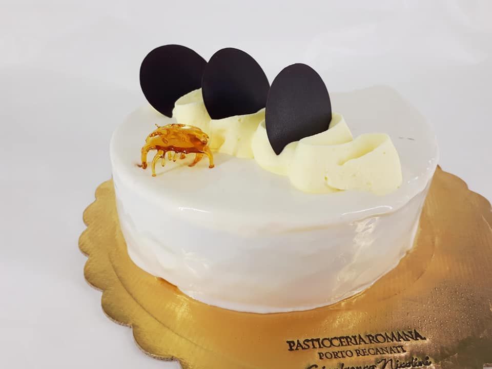 Una torta ricoperta di glassa bianca, decorata con tre dischi di cioccolato fondente, panna montata e una guarnizione al caramello, su un vassoio dorato.