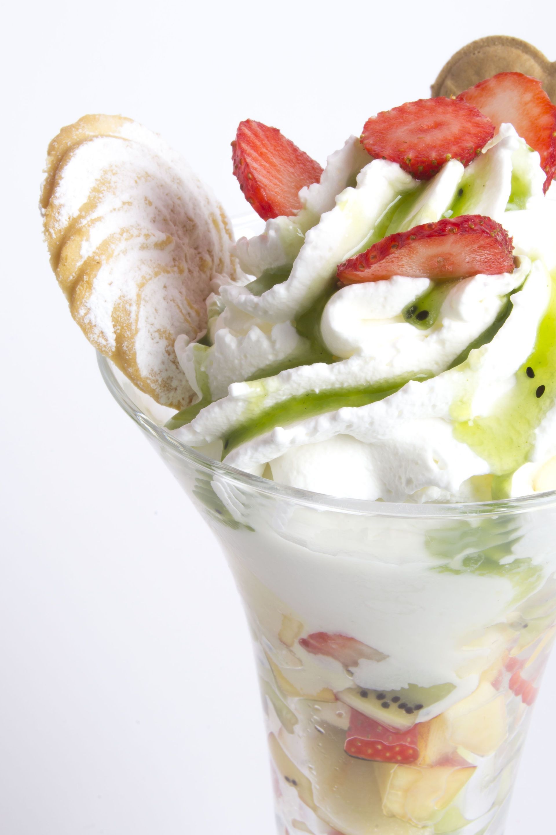 Un parfait di frutta in un bicchiere alto, guarnito con panna montata, fragole a fette, kiwi e una grande meringa.