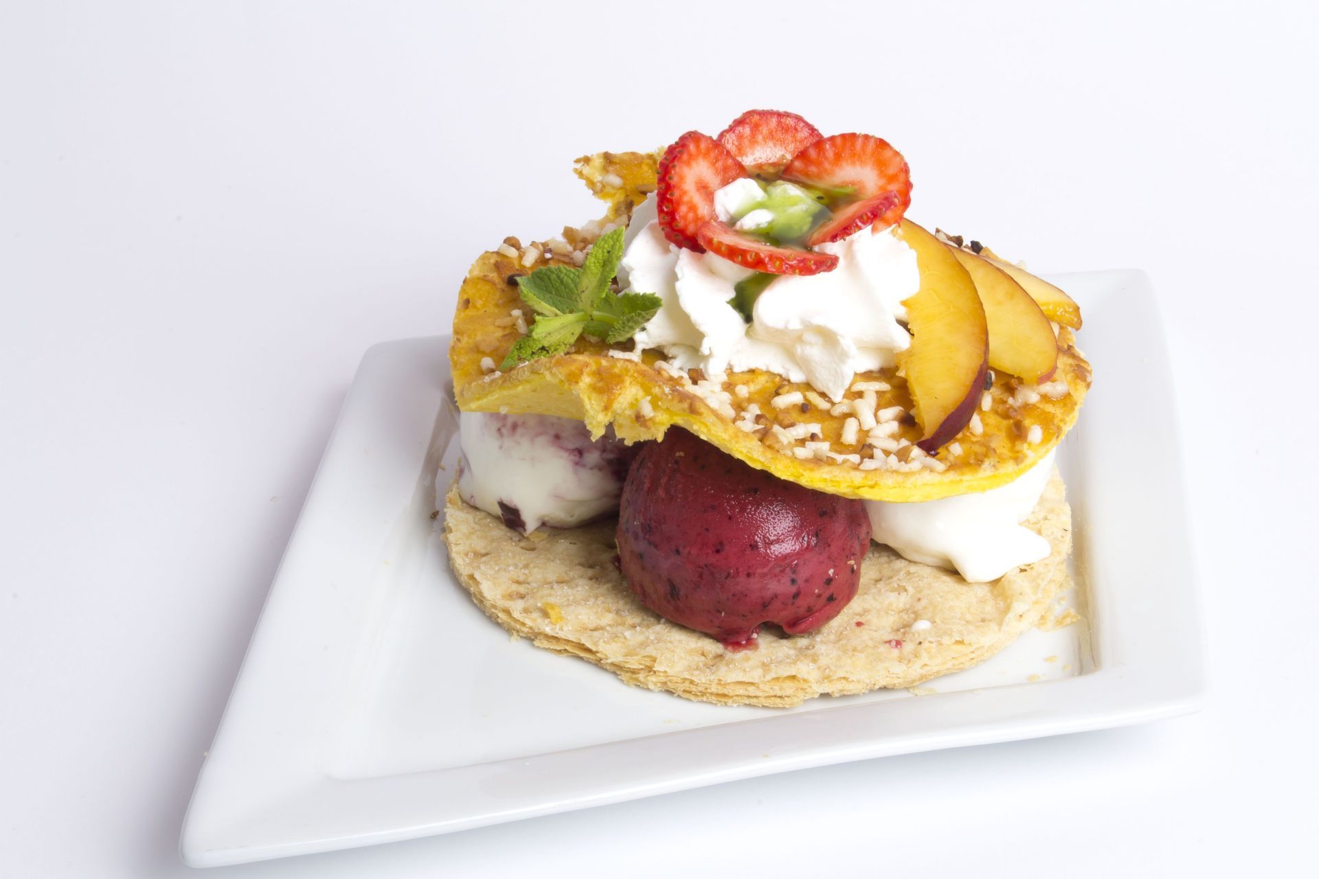 Un sandwich dolce con gelato, sorbetto, frutta, panna montata e menta su un piatto bianco su sfondo bianco.