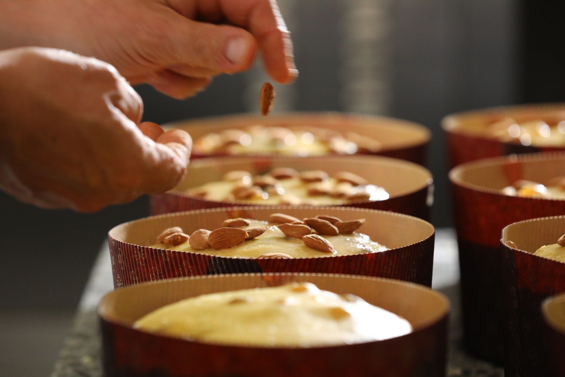 Una mano posiziona le mandorle sopra l'impasto in diversi stampini rotondi rivestiti di carta da forno.