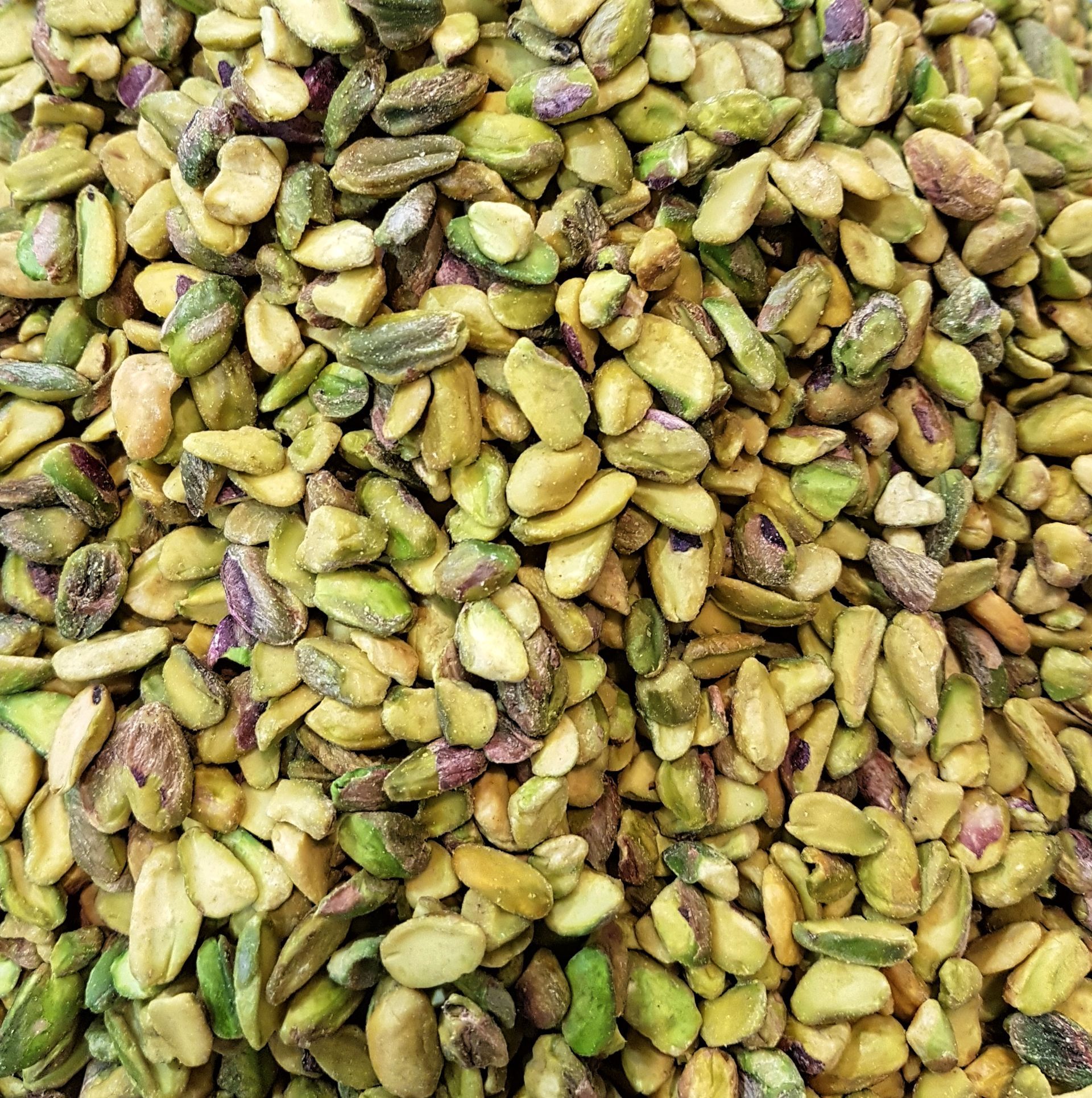 Una vista ravvicinata di numerosi pistacchi sgusciati, di colore verde chiaro e giallastro.