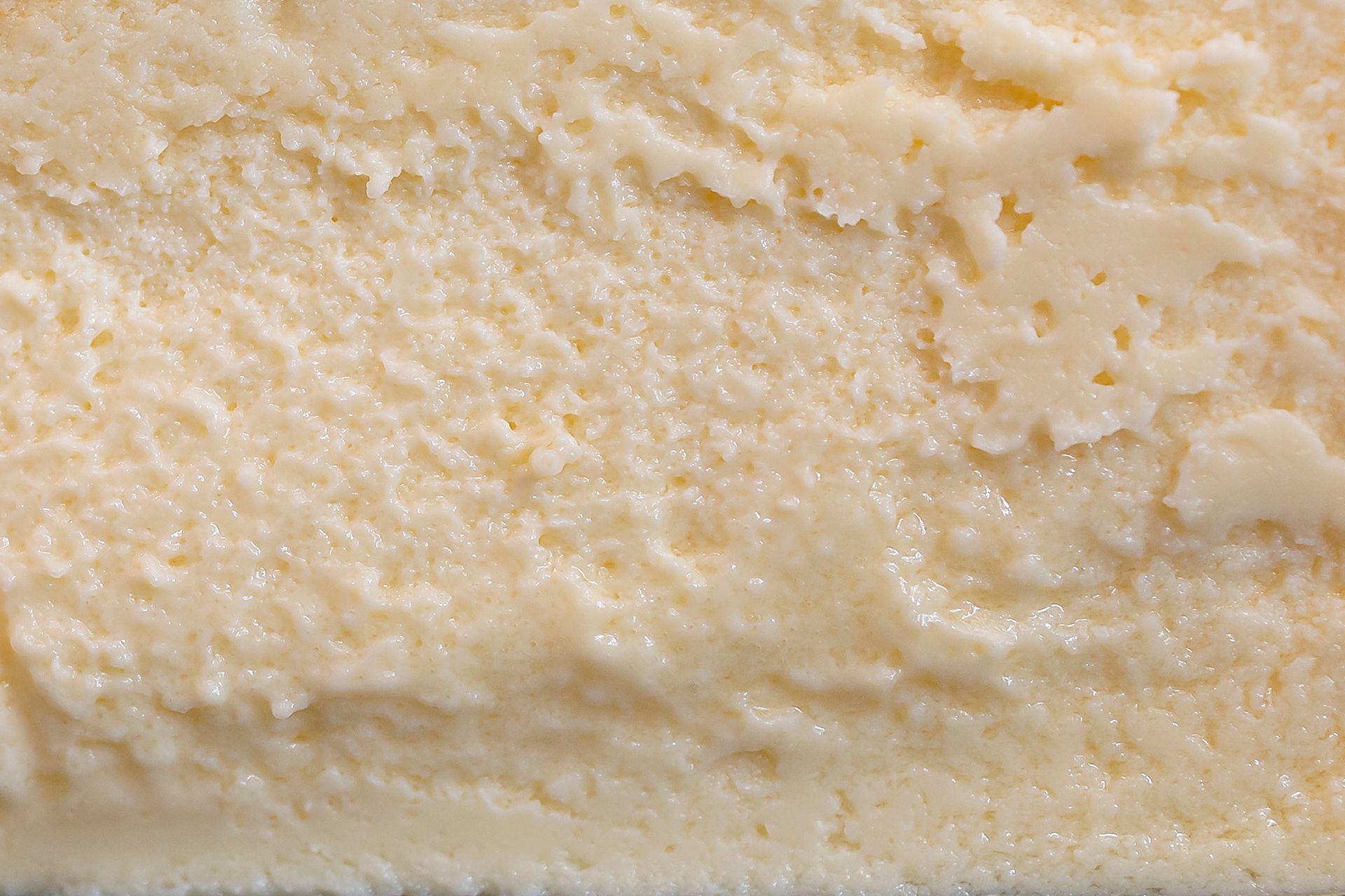 Un'immagine ravvicinata, macro, della consistenza cremosa, giallo pallido e granulosa del formaggio.