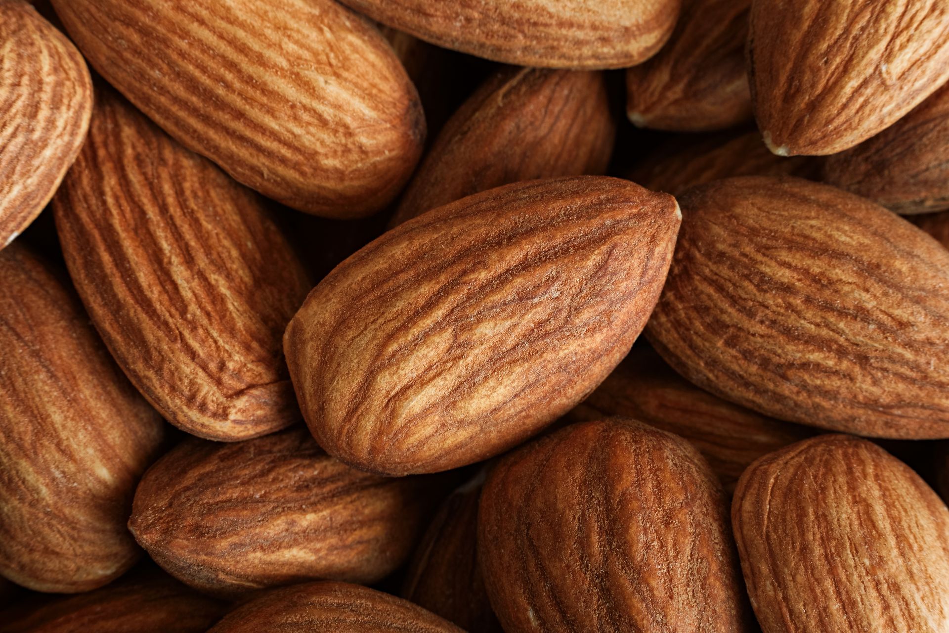 Una vista ravvicinata di numerose mandorle intere e crude, con la buccia ben visibile, ammassate l'una sull'altra.