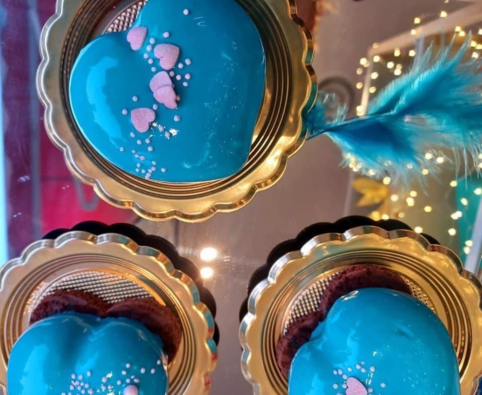 Tre torte a forma di cuore glassate di un blu acceso, decorate con minuscoli cuoricini rosa e zuccherini colorati su piatti dorati.