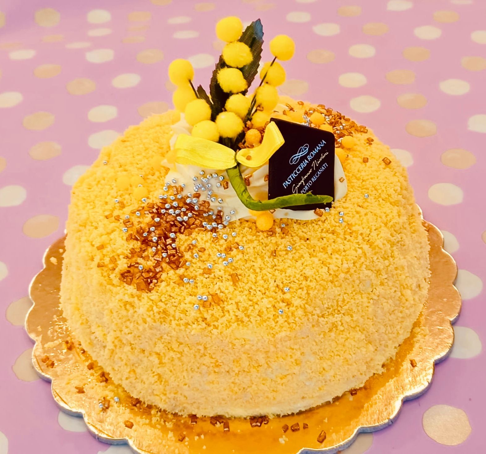 Primo piano di una torta giallo brillante, ricoperta di briciole e decorata con una spirale di panna e scaglie di cioccolato fondente.