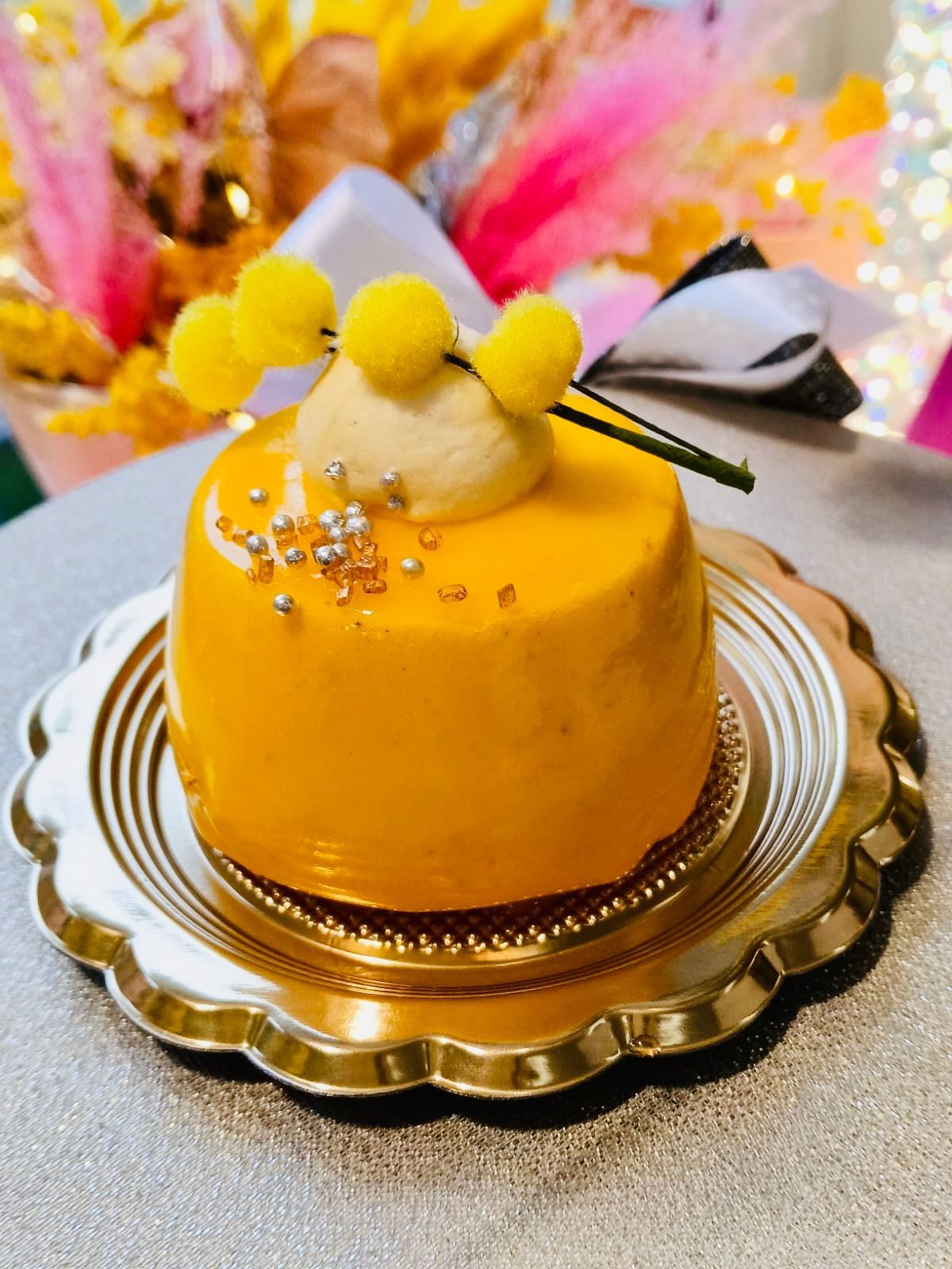 Una piccola torta rotonda di colore giallo, guarnita con una cucchiaiata di panna e scaglie di cioccolato, su uno sfondo bianco.