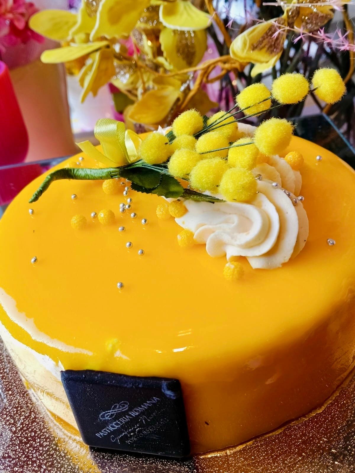 Una piccola torta rotonda di colore giallo, guarnita con una cucchiaiata di panna e scaglie di cioccolato, su uno sfondo bianco.
