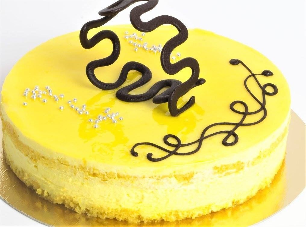 Primo piano di una torta giallo brillante, ricoperta di briciole e decorata con una spirale di panna e scaglie di cioccolato fondente.