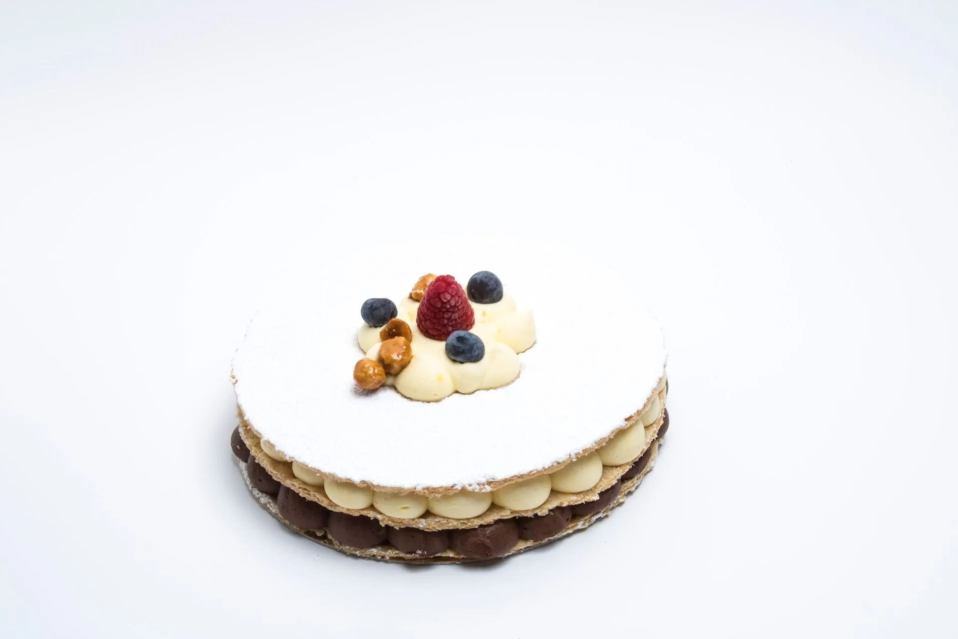 Un dessert a strati con cioccolato e panna, ricoperto di glassa bianca, lamponi, mirtilli e noci.