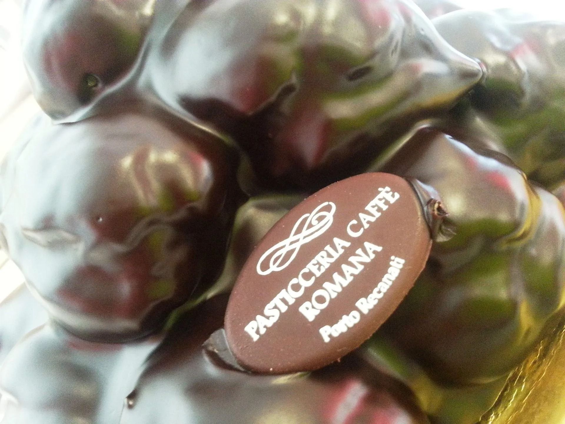 Un bignè ricoperto di crema al cioccolato, sormontato da una targhetta con il marchio Pasticceria Caffè Romana di Porto Recanati.